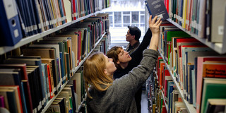 Students search for books on bookshelves in the library.
